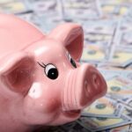 Pink piggy bank sitting on a pile of hundred-dollar bills