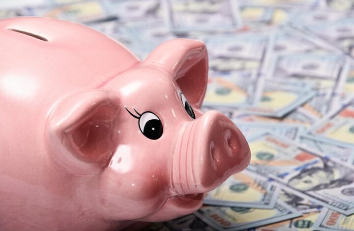 Pink piggy bank sitting on a pile of hundred-dollar bills
