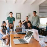 Group of young professionals collaborating around laptops in a bright, modern office setting.