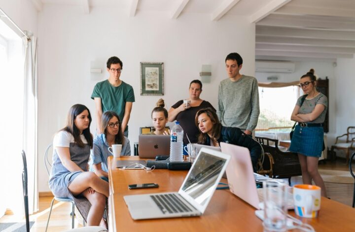 Group of young professionals collaborating around laptops in a bright, modern office setting.