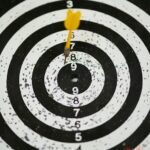 A yellow dart hitting the bullseye on a black and white target, symbolizing precise funding goals set with crowdfunding benchmarks.